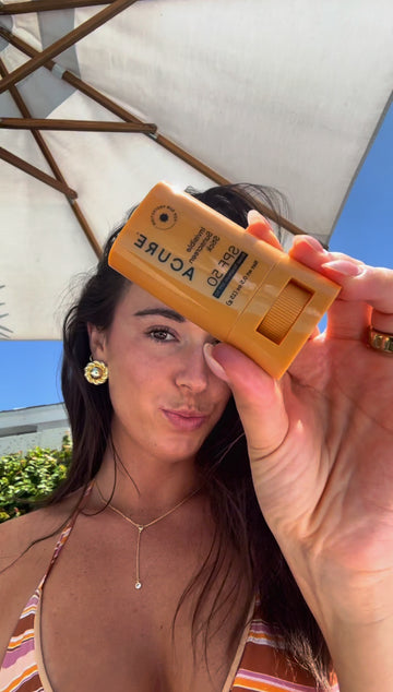 Woman holding a sunscreen bottle under an umbrella with a clear blue sky in the background